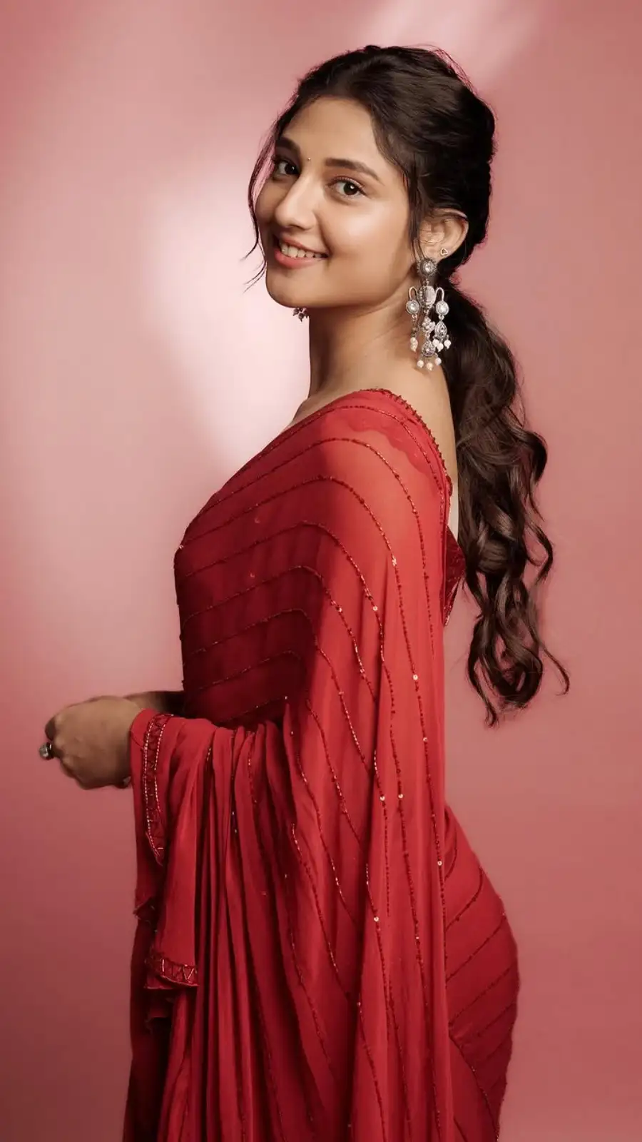 Ritika Nayak smiling in a red sari against a pink backdrop